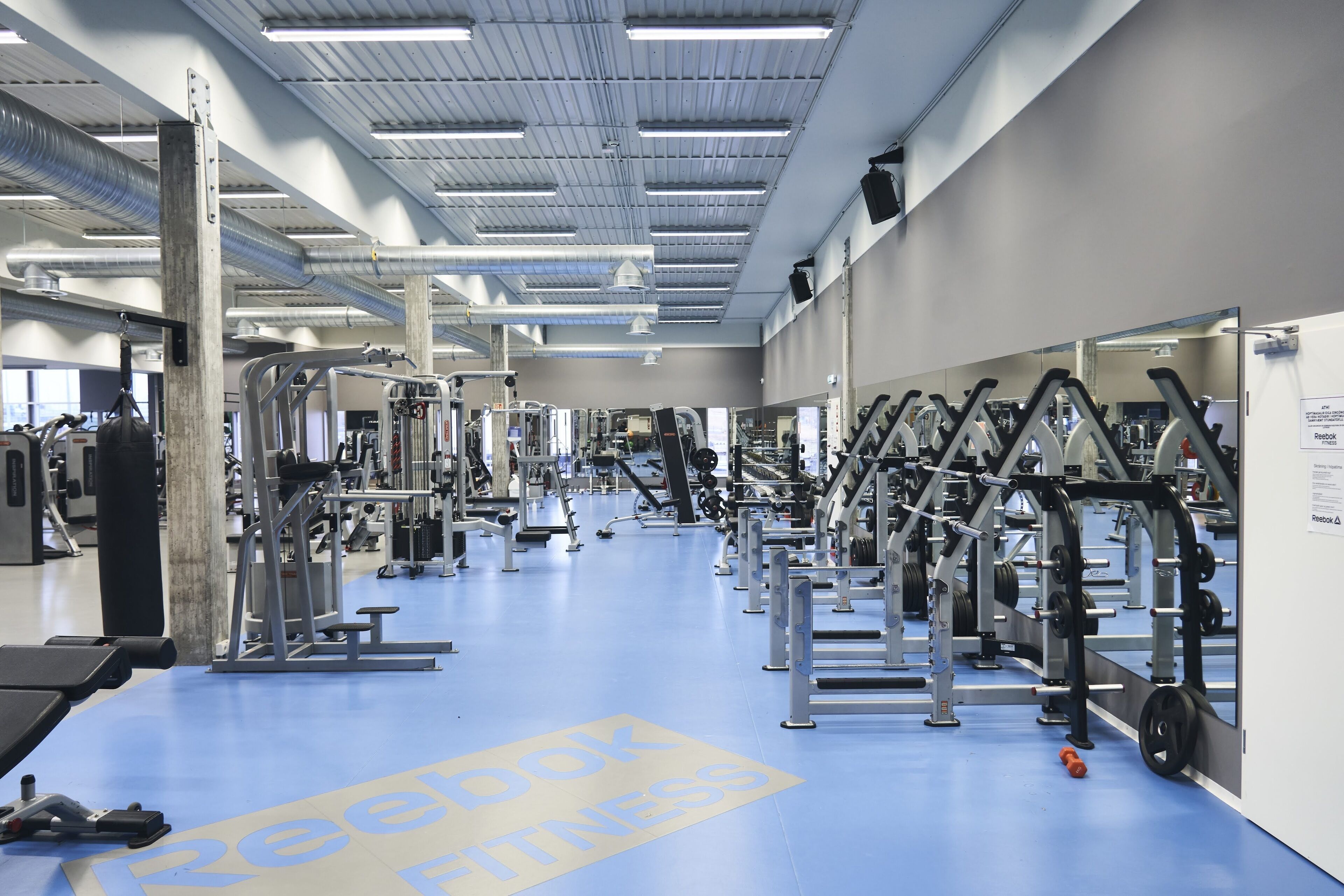 A gym with various exercise equipment, a blue floor, and a Reebok Fitness logo.