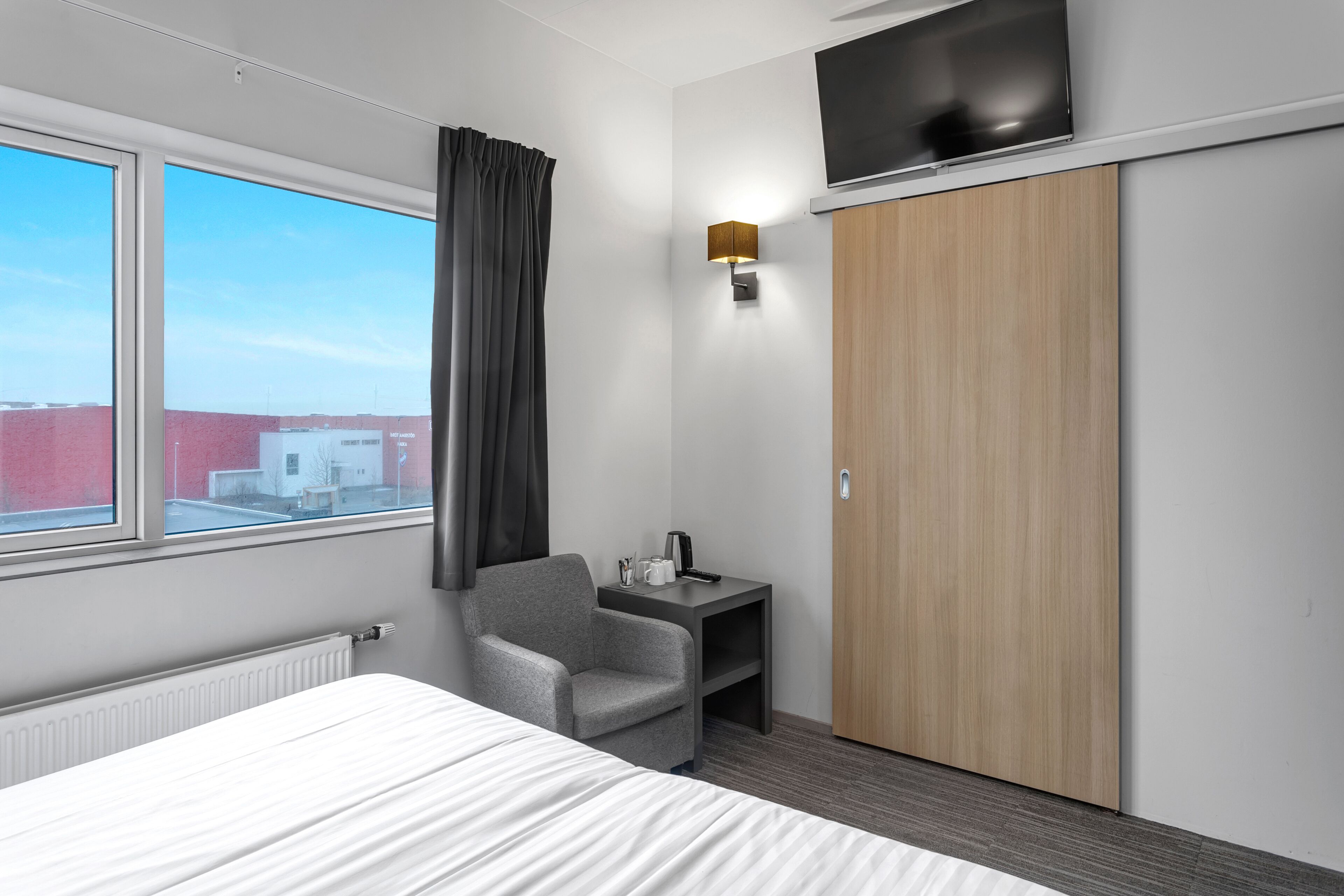 A hotel room with a bed, a desk with a lamp, a TV, and a wardrobe.