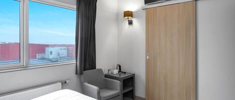 A hotel room with a bed, a desk with a lamp, a TV, and a wardrobe.