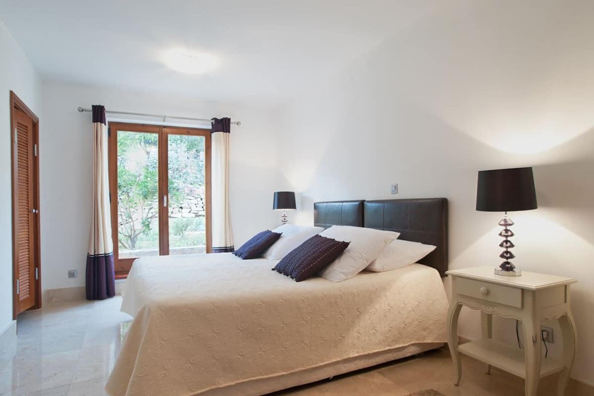 Une chambre à coucher avec un lit, une table de chevet, une lampe et une fenêtre avec des rideaux.