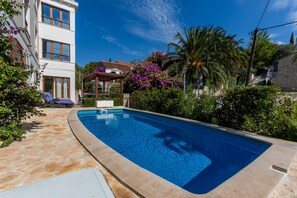 Relax by the serene pool surrounded by lush greenery and a shaded seating area.
