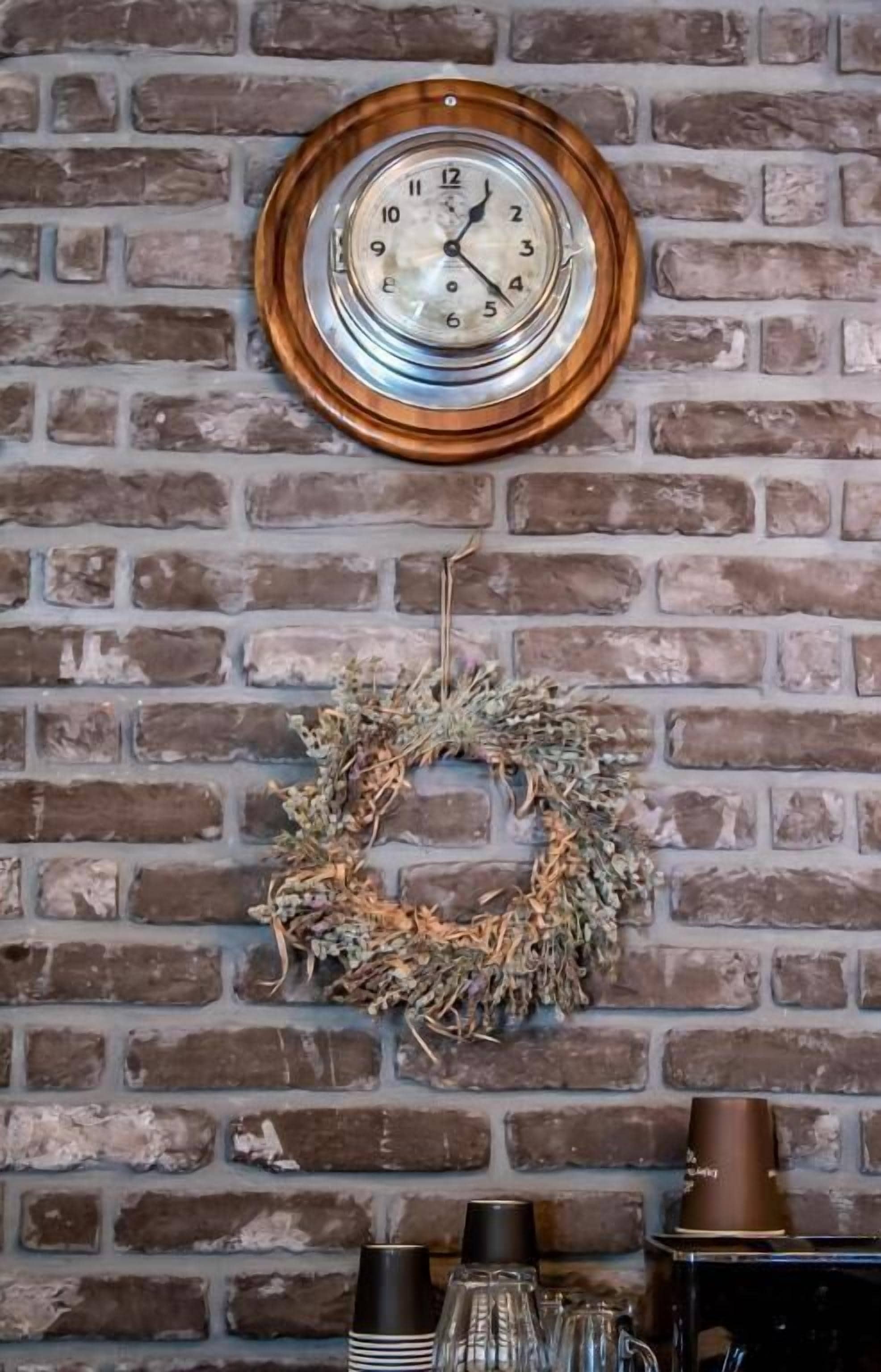Un muro de ladrillo con un reloj y un adorno floral.