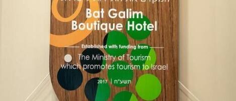A wooden sign with Hebrew text and a logo for Bat Galim Boutique Hotel, established with funding from The Ministry of Tourism.