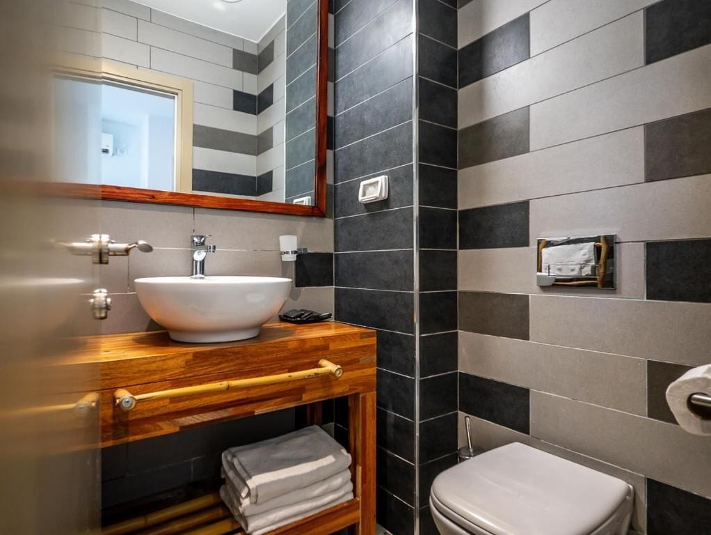 Ein Badezimmer mit einem Holzkosmetikschrank, einem weißen Waschbecken, einem Spiegel, einer Toilette und einem Handtuchhalter.