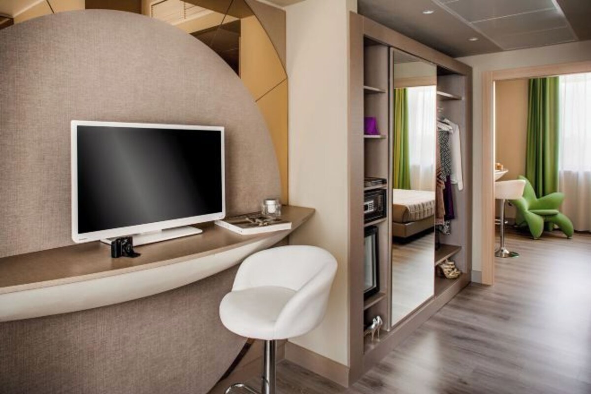 Una habitación de hotel moderna con televisión de pantalla plana, una silla blanca, una cama y una silla verde.