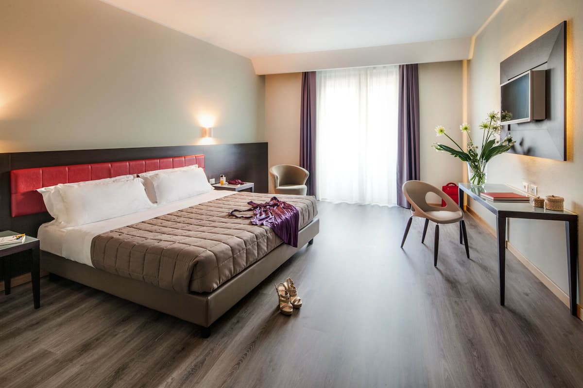 A modern hotel room with a large bed, a desk, a chair, and a TV mounted on the wall.