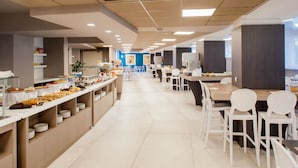 A spacious cafeteria with multiple tables and chairs, a variety of food items on display, and a clean, modern design.