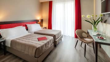 Habitación de hotel con dos camas, un escritorio con una computadora portátil, una silla y un florero con flores.