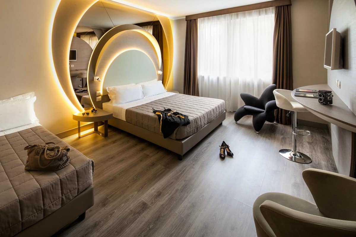 A modern hotel room with a large bed, a desk, a chair, and a television.