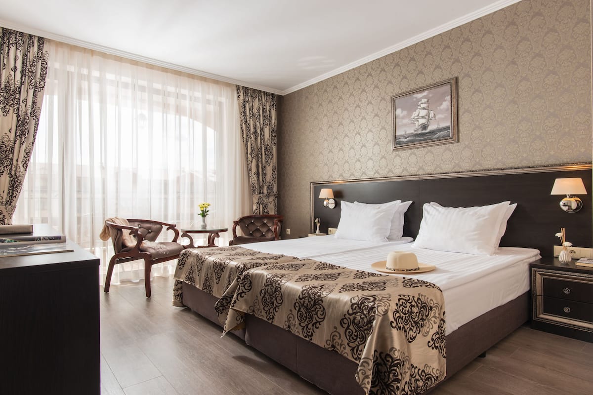 A hotel room with a large bed, a desk, a chair, and a nightstand.