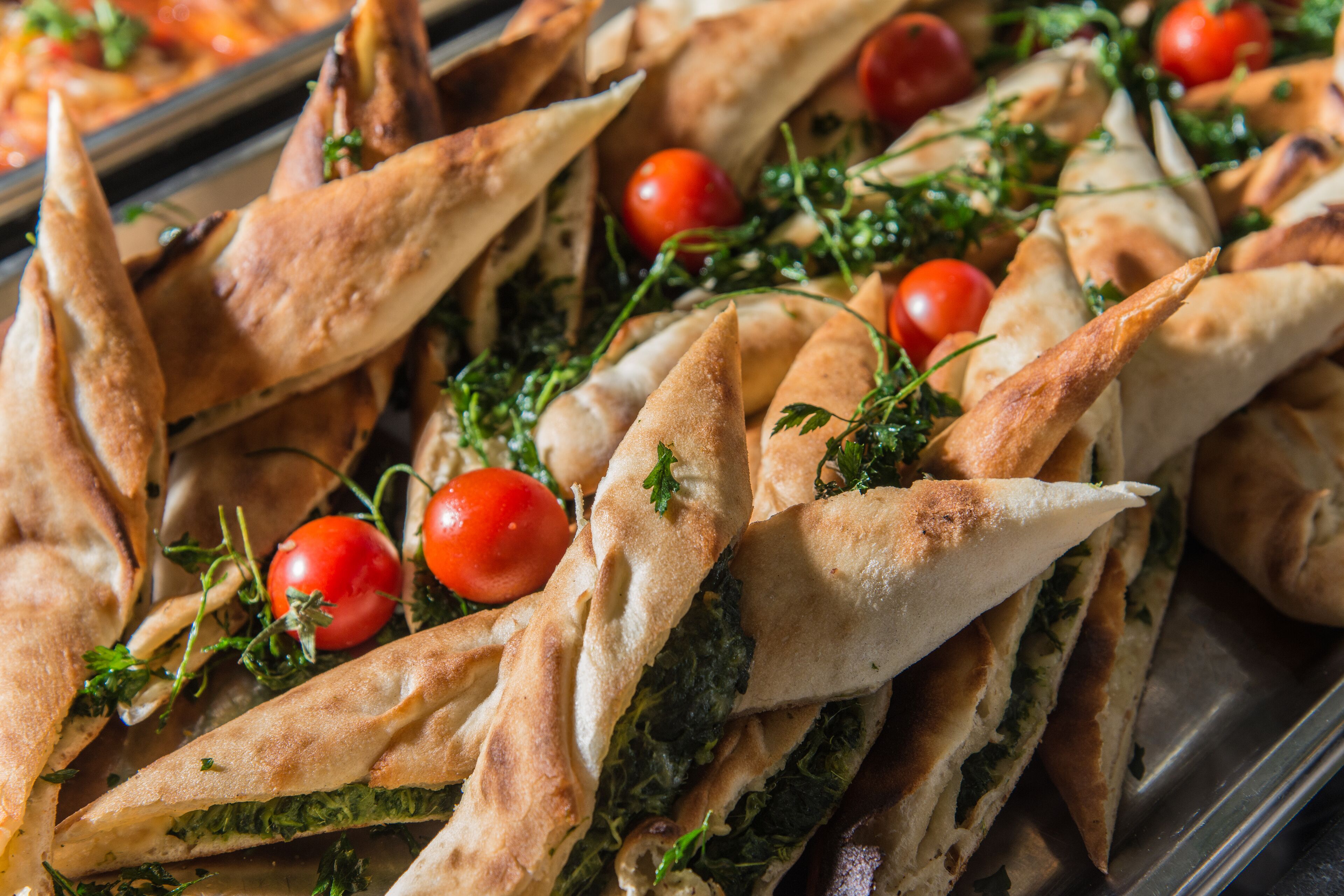 A tray of triangular pastries with a filling, garnished with cherry tomatoes and herbs.