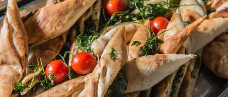 A tray of triangular pastries with a filling, garnished with cherry tomatoes and herbs.