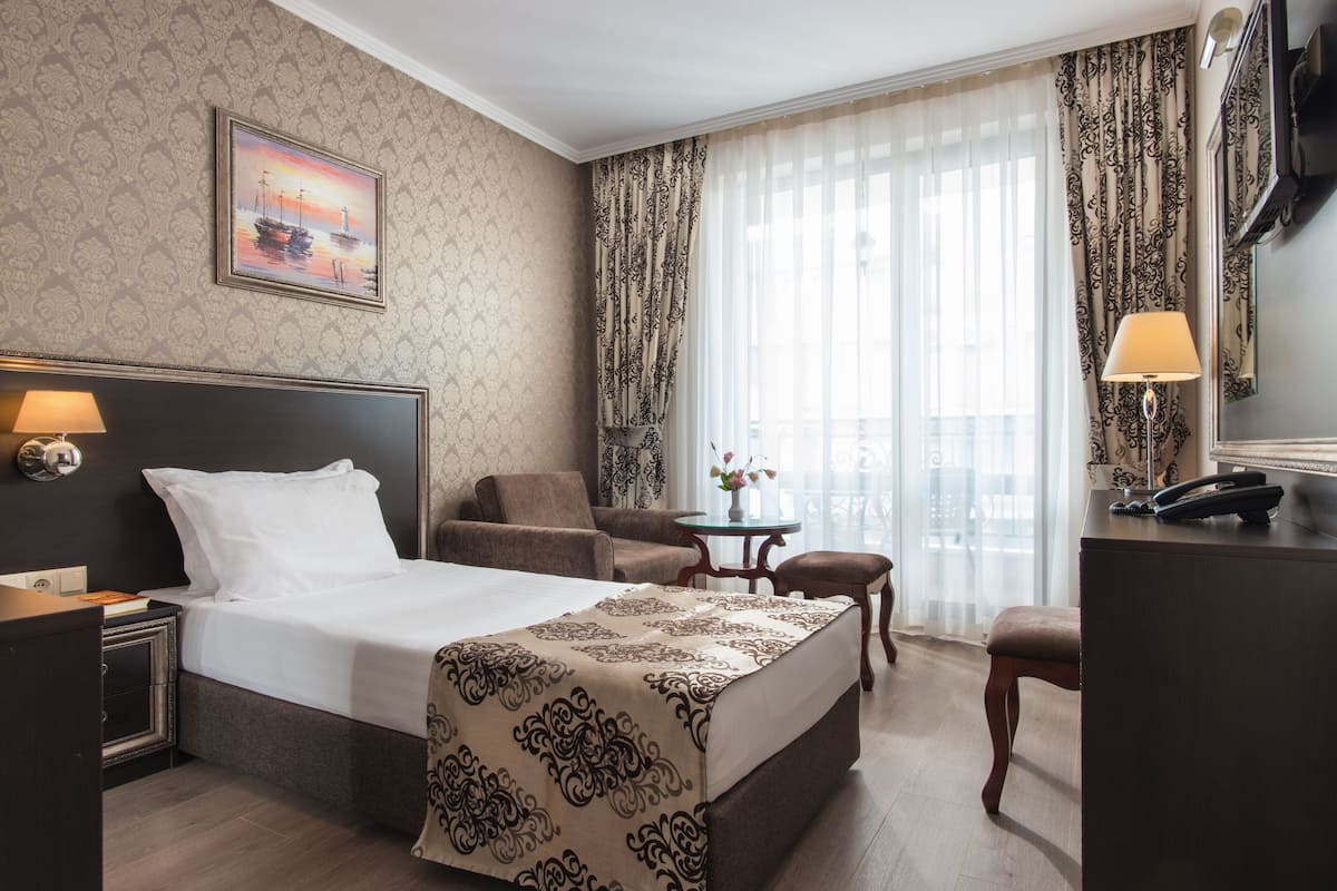 A hotel room with a large bed, a desk, a chair, a small table, and a window with curtains.