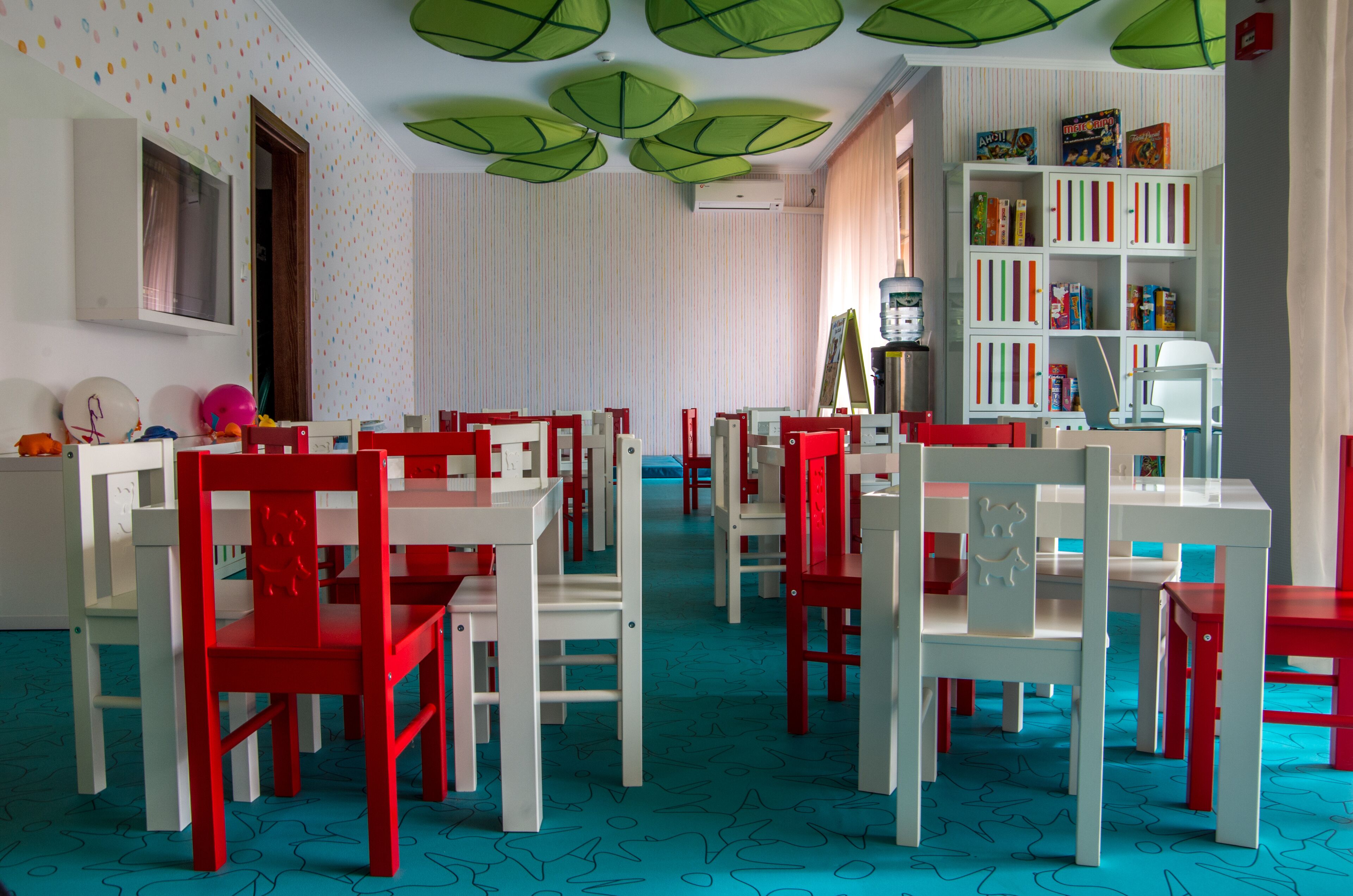 A children's playroom with red and white furniture, a bookshelf, and patterned carpet.