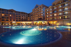 A hotel with a large swimming pool, multiple balconies, and outdoor seating areas.
