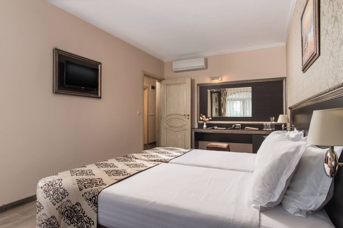 A hotel room with a bed, a desk, a mirror, and a television.