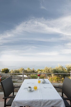 An outdoor dining table with a white tablecloth, set with a cup, a glass of orange juice, and a vase with flowers. - Alonissos Beach Bungalows & Suites Hotel (Alonissos)
