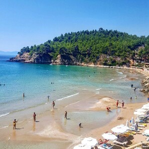 A beach with clear water, people swimming and walking, and umbrellas on the sand. - Alonissos Beach Bungalows & Suites Hotel (Alonissos)