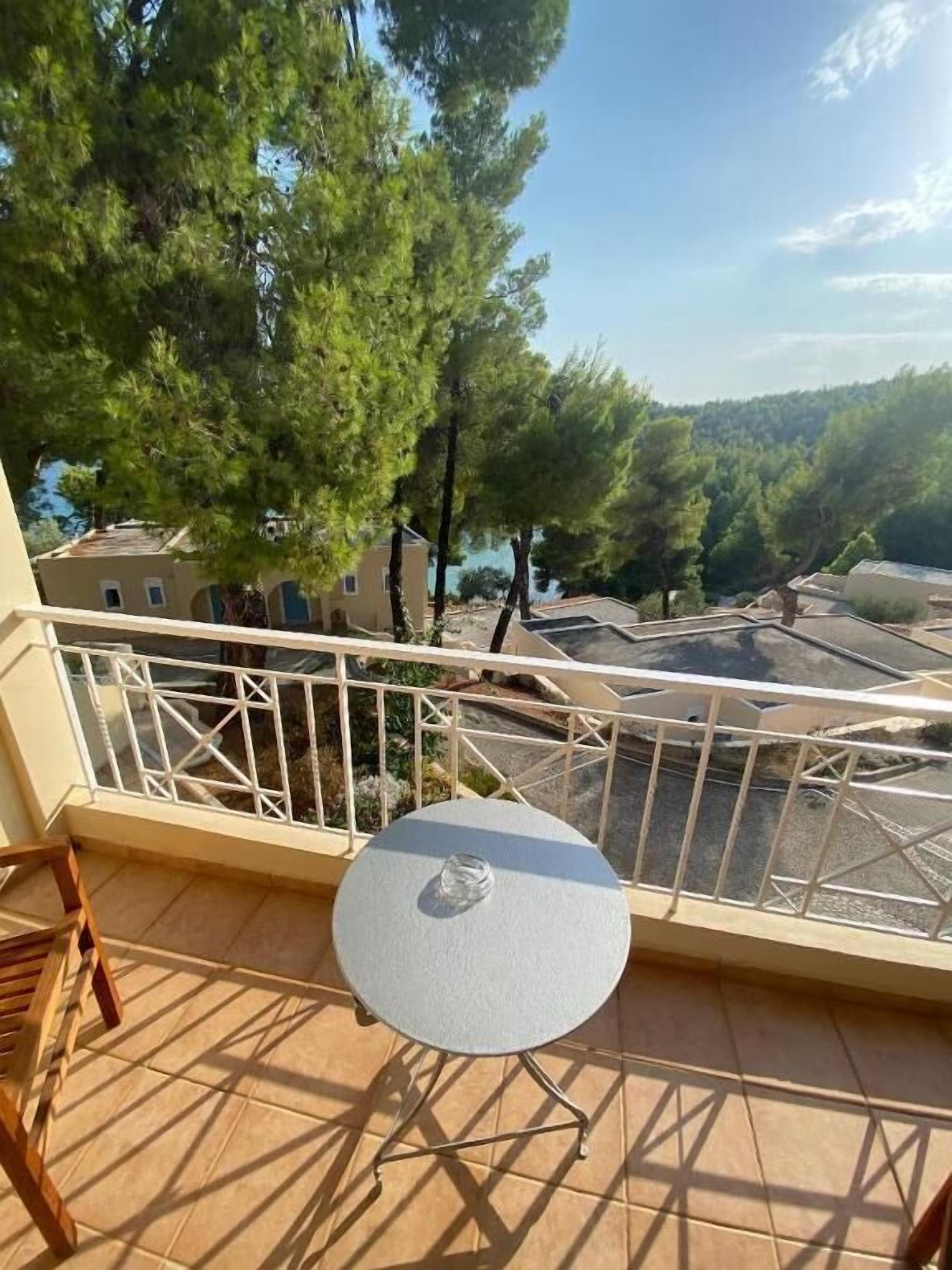 Un balcon avec une table ronde et des chaises, donnant sur un quartier résidentiel bordé d’arbres et de maisons.