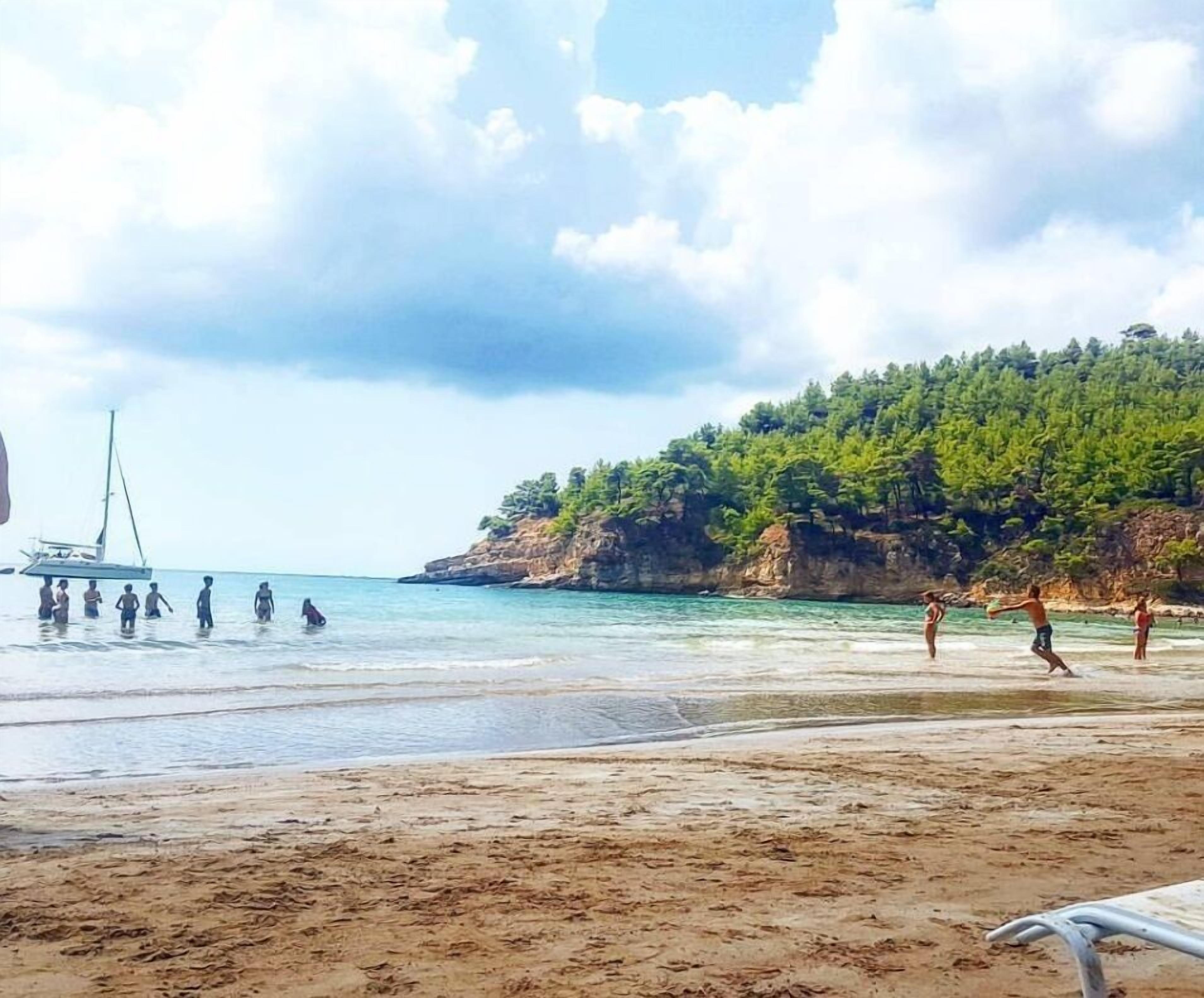 A beach with clear water, a sailboat, and people enjoying the shore.