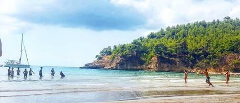 A beach with clear water, a sailboat, and people enjoying the shore.