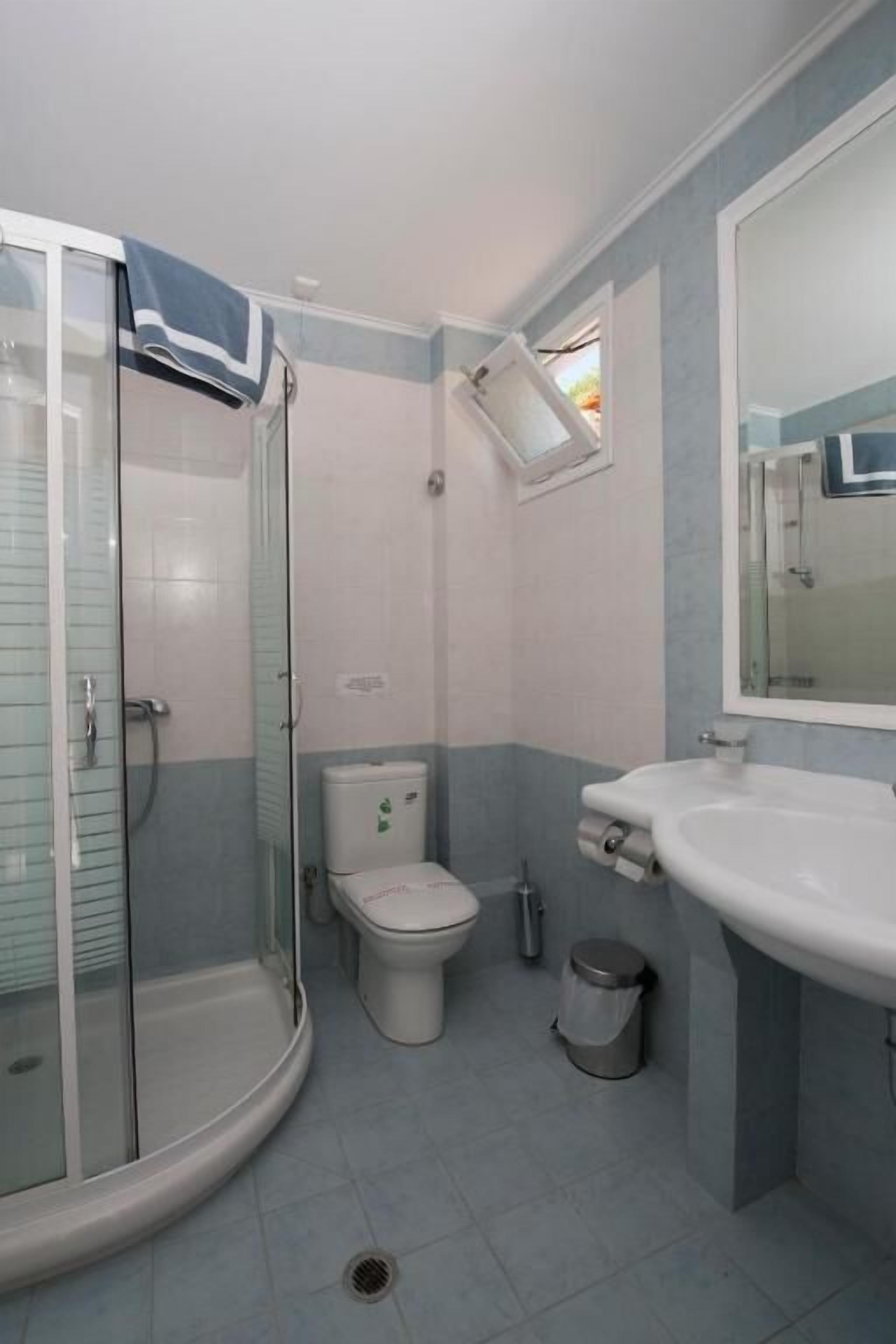 A bathroom with a glass shower enclosure, a toilet, a sink, and a mirror.