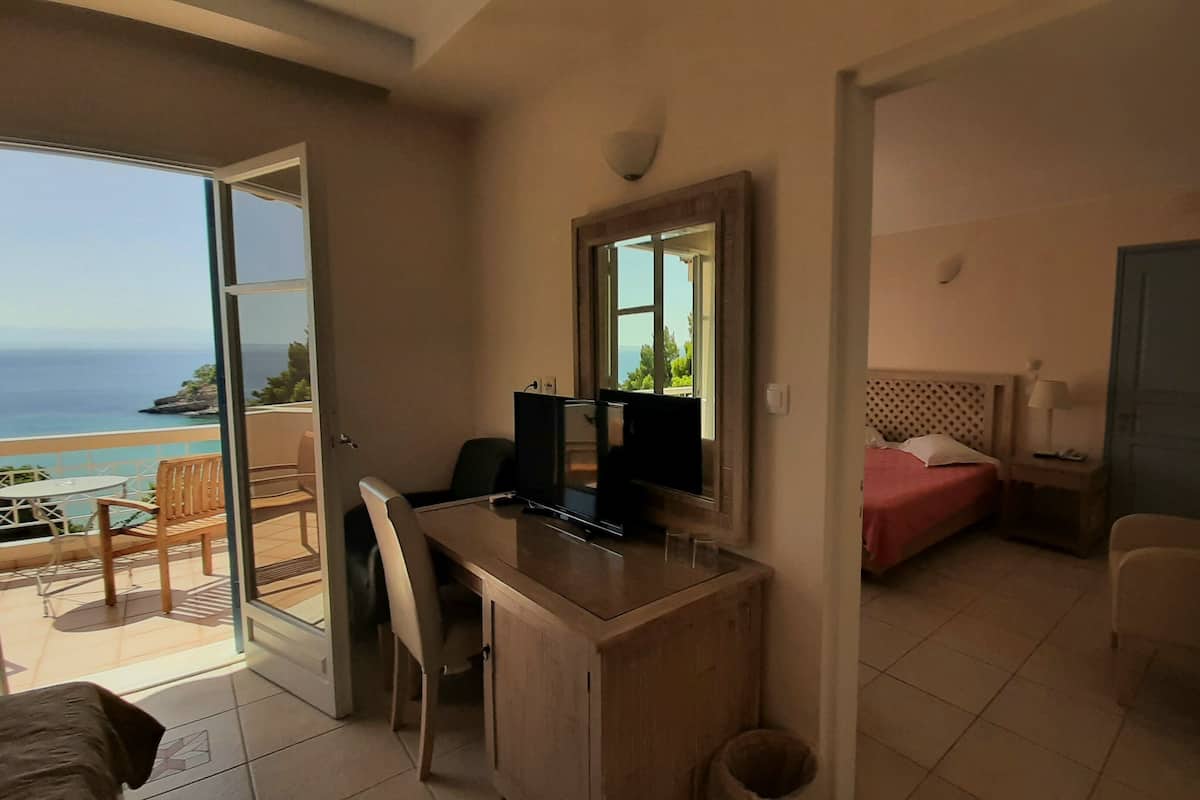 Ein Hotelzimmer mit Schreibtisch, Bett, Fernseher und einem Balkon mit Meerblick.