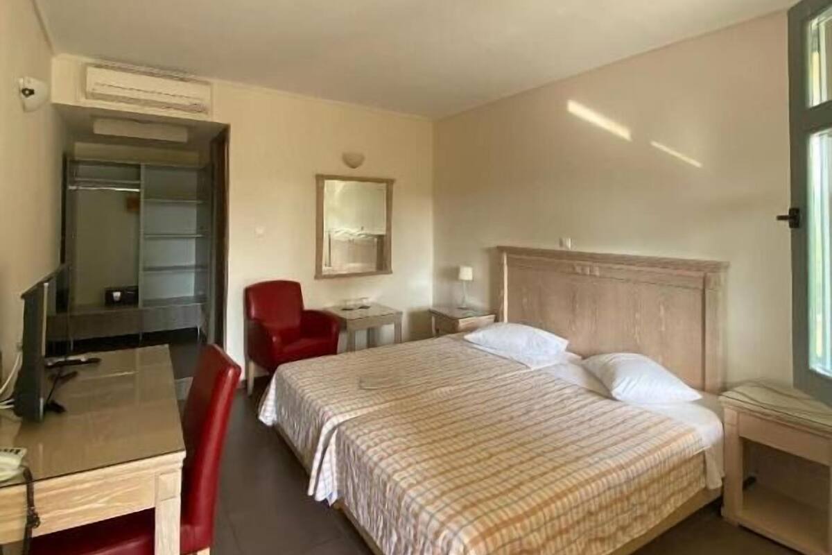 Ein Hotelzimmer mit Bett, Schreibtisch, Stuhl, Spiegel und Fenster.