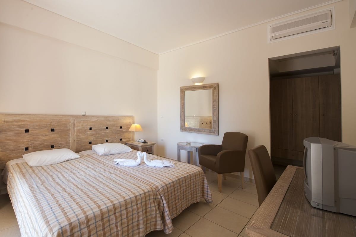 Ein Hotelzimmer mit zwei Betten, einem Schreibtisch, einem Stuhl, einem Fernseher und einem Spiegel.