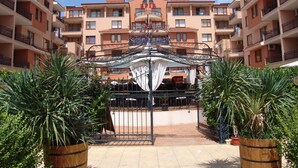A courtyard with a wrought iron gate, surrounded by potted plants and a building with balconies in the background. - Apart-hotel Efir (Sunny Beach)
