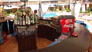 A bar area with a pool view, bar stools, and a Coca-Cola cooler. - Apart-hotel Efir (Sunny Beach)