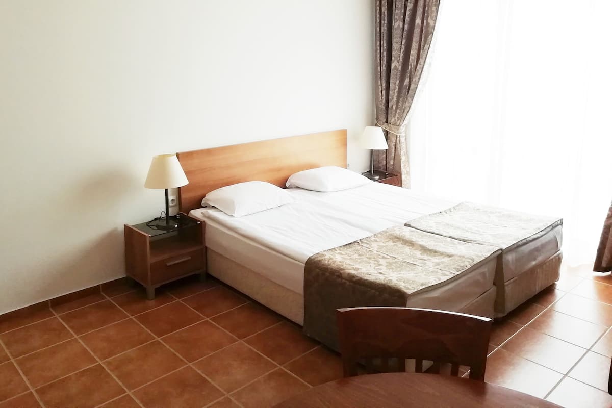 A hotel room with a bed, two bedside lamps, a nightstand, a chair, and a window with curtains.