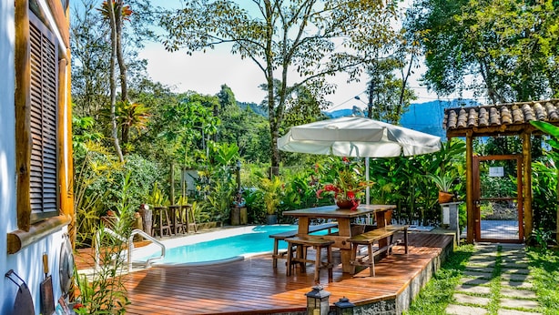 A wooden deck with a pool, surrounded by lush greenery and a pergola with an umbrella. - Pousada Estalagem Paraty (Paraty)