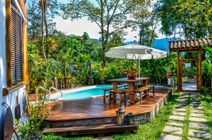 A wooden deck with a pool, surrounded by lush greenery and a pergola with an umbrella. - Pousada Estalagem Paraty (Paraty)