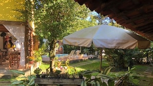 A patio area with a wooden table and chairs, surrounded by potted plants and a large umbrella. - Pousada Estalagem Paraty (Paraty)