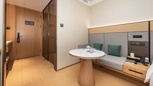 A hotel room with a wooden door, a small round table with a white top, a sofa with cushions, and a bedside table with a lamp and a remote control. - Ji Hotel (Shanghai)