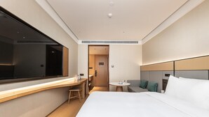 A hotel room with a bed, a desk, a chair, a small table, and a window. - Ji Hotel (Shanghai)