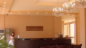 A reception area with a reception desk, a chandelier, a sofa, and a sign that reads "RECEPTION HAPPY". - Apart-hotel Happy (Sunny Beach)