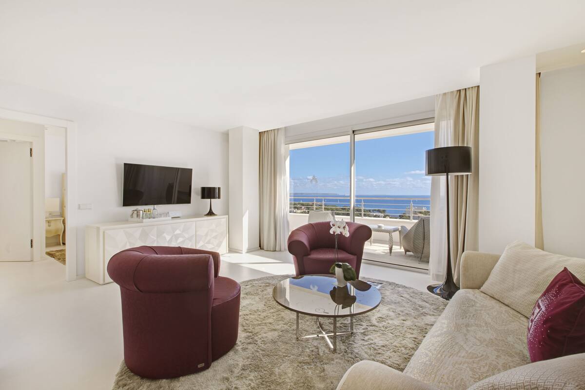 A modern living room with a large window offering a view of the sea, a flat-screen TV, and a white console table.
