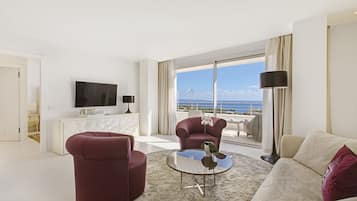 Una sala de estar moderna con un ventanal que ofrece vistas al mar, un televisor de pantalla plana y una consola blanca.