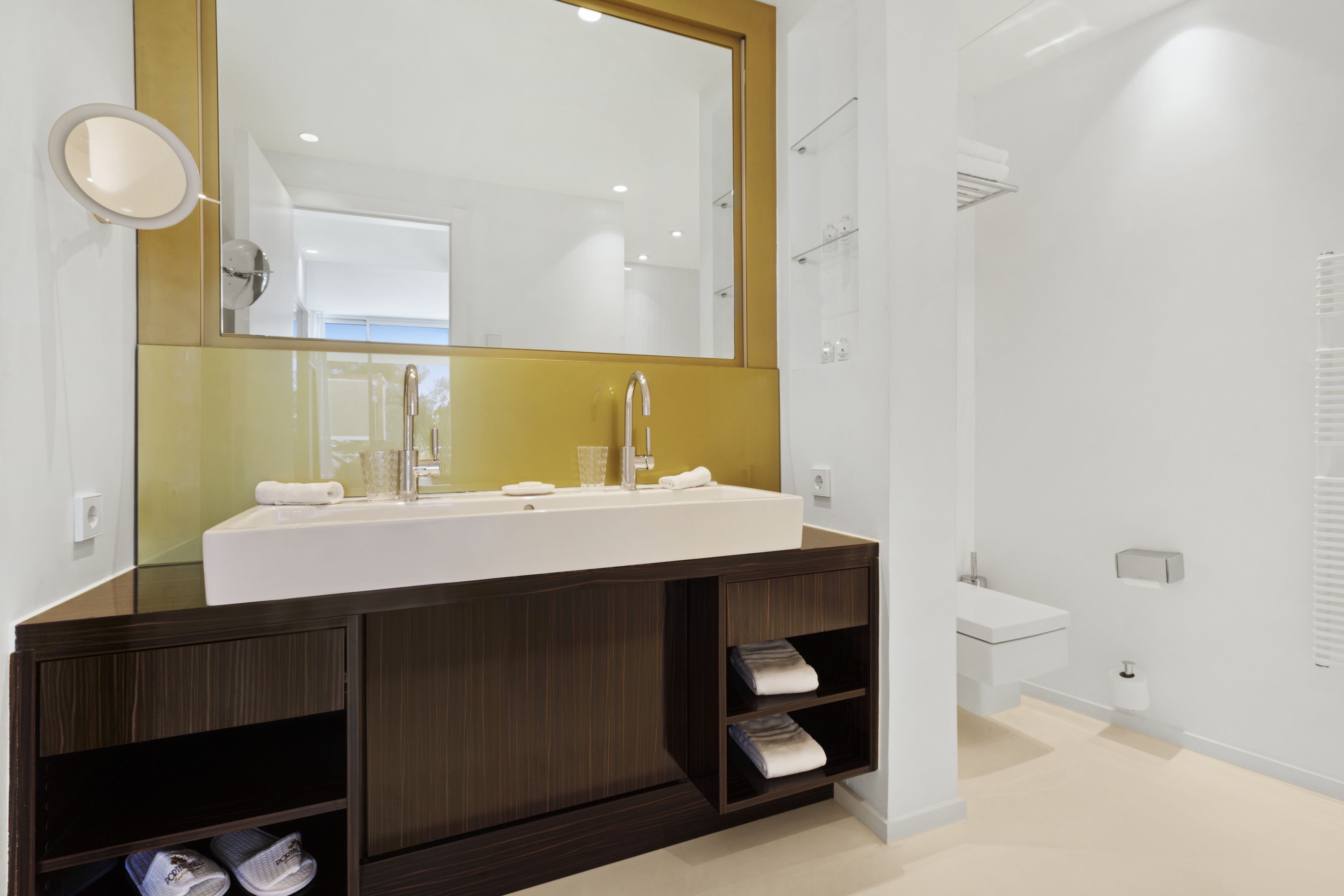A modern bathroom with a large mirror, a white sink, and a dark wooden vanity.
