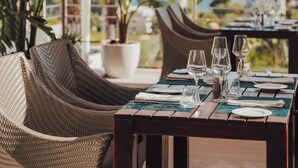 An outdoor dining area with wicker chairs and tables, a potted plant, and a view of the ocean. - Portals Hills Boutique Hotel (Calvia)