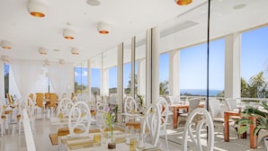A spacious dining area with white furniture, large windows, and a view of the sea. - Portals Hills Boutique Hotel (Calvia)