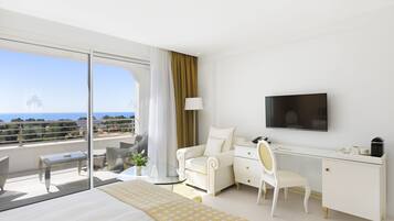 A modern hotel room with a large bed, a desk, a chair, a TV, and a balcony with a view of the ocean.