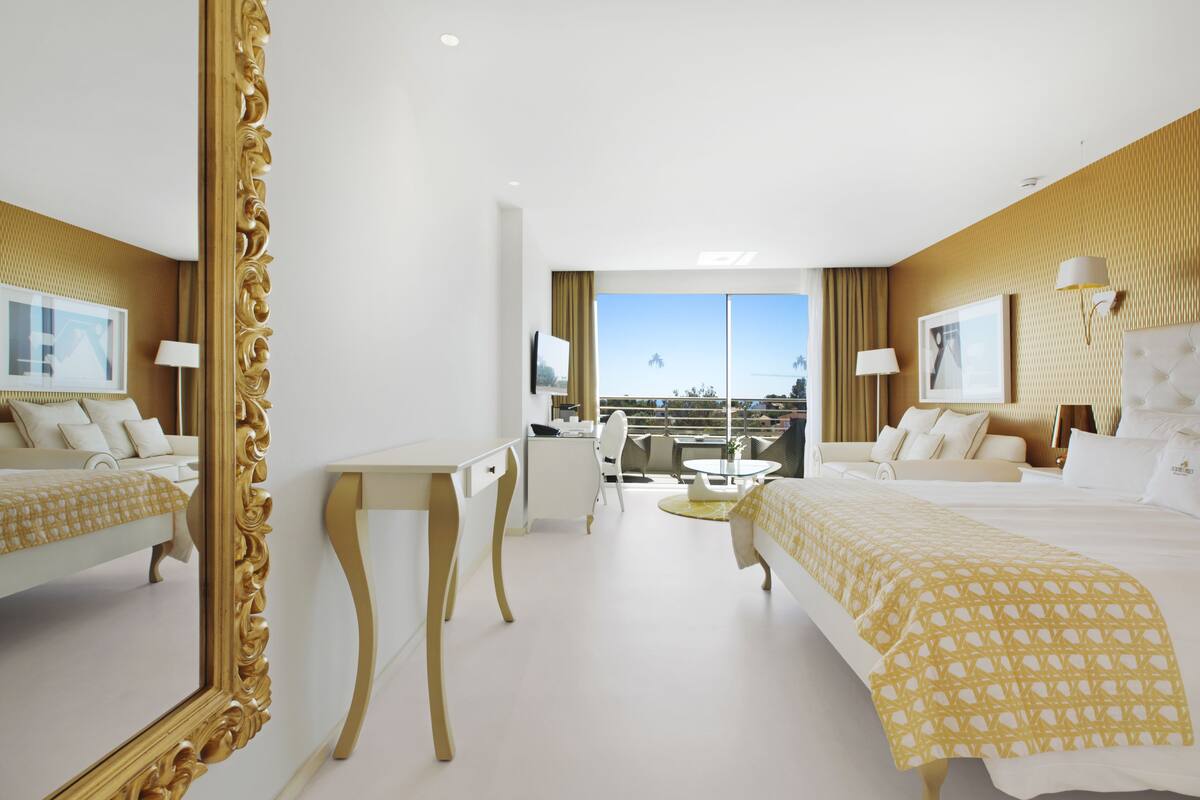 A hotel room with a large bed, a desk, a chair, and a balcony with a view.
