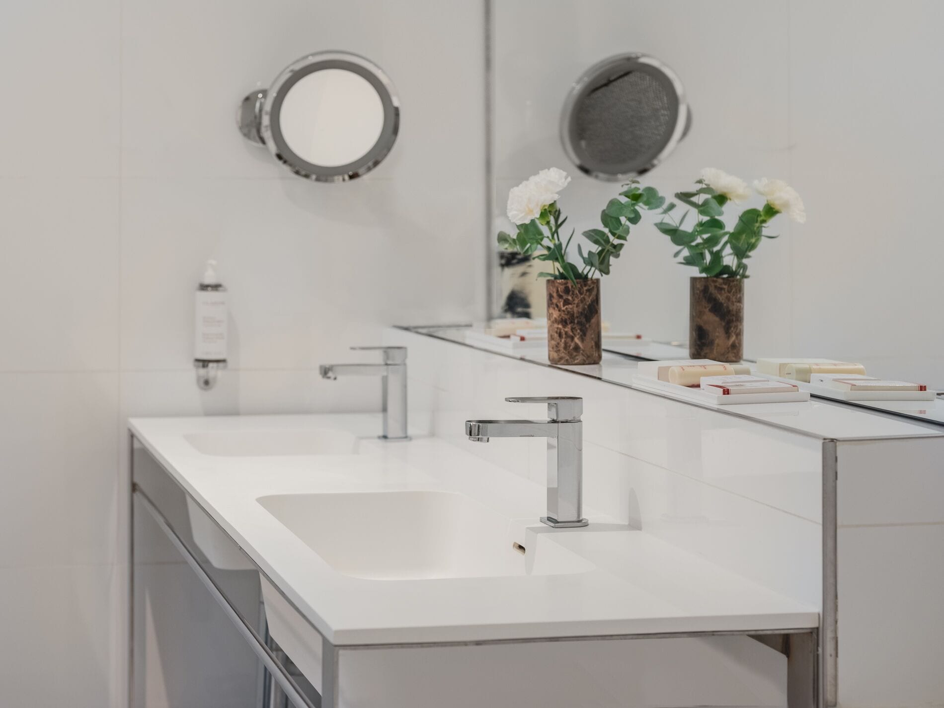 A modern bathroom with a white sink, a mirror, and two vases with white flowers.