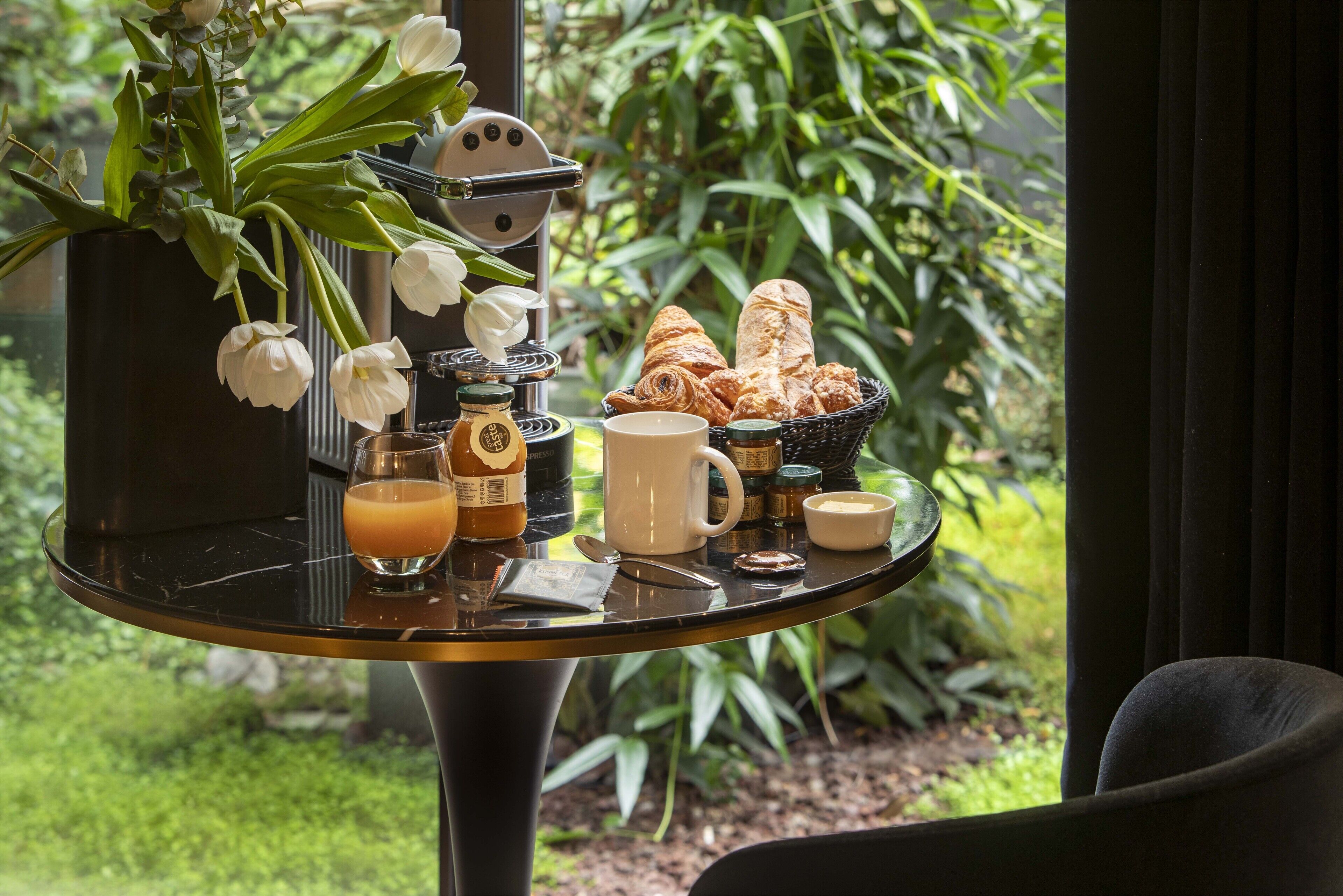 A breakfast table with croissants, a coffee pot, a cup, and a vase of flowers.