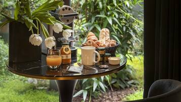 A breakfast table with croissants, a coffee pot, a cup, and a vase of flowers.