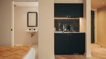 A modern hotel room with a bed, a bathroom with a sink and mirror, and a kitchenette area.