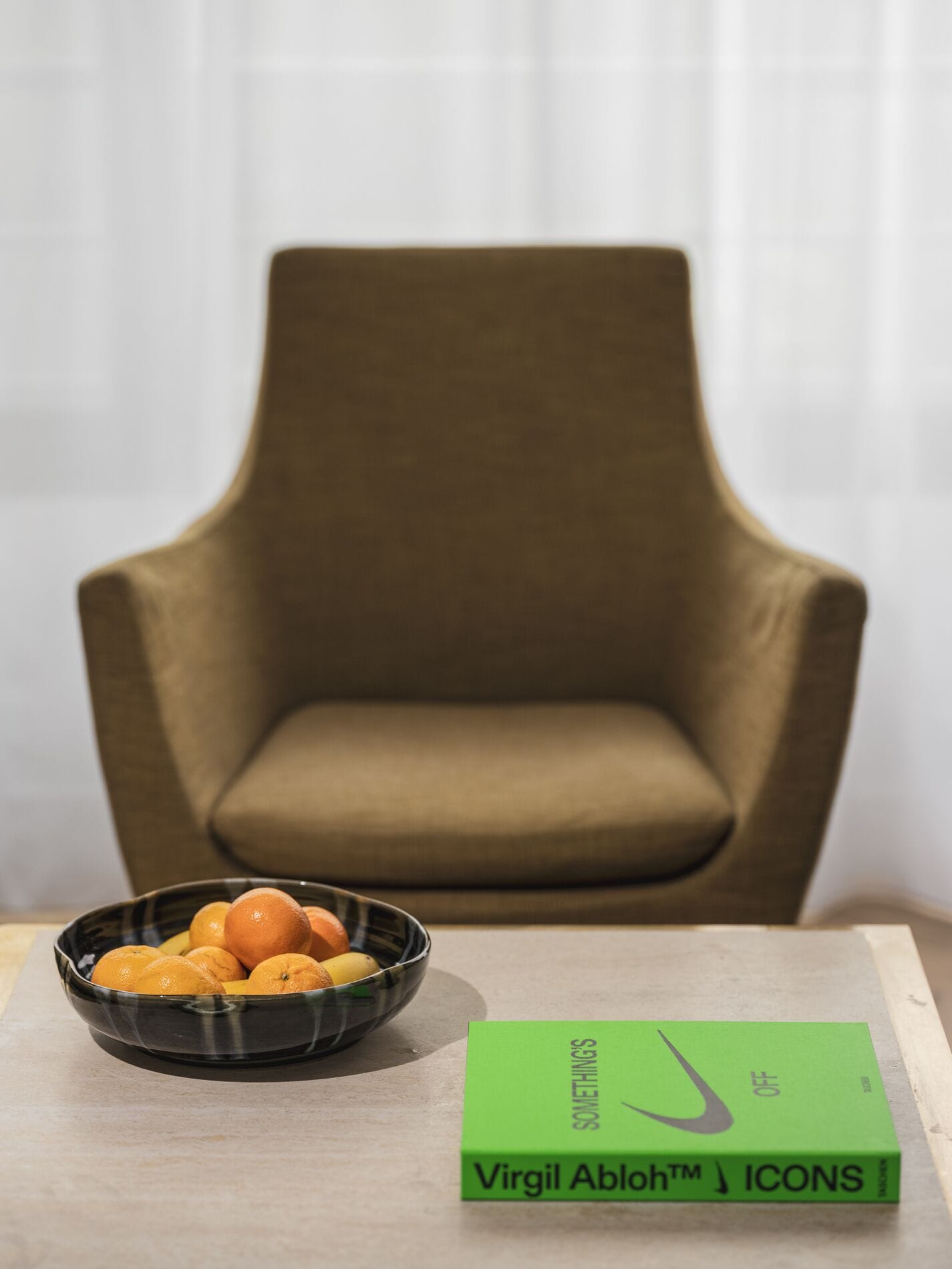 A green book titled 'Virgil Abloh™ ICONS' on a table with a bowl of oranges.
